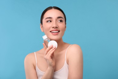 Beautiful woman with makeup remover and cotton pad on light blue background