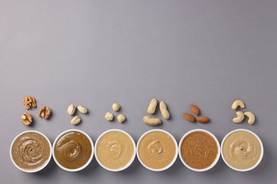 Many tasty nut butters in bowls and nuts on grey table, flat lay. Space for text