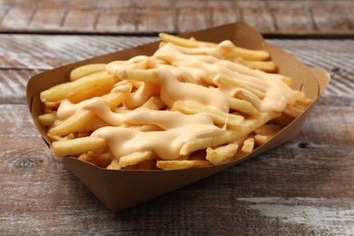 Photo of Delicious French fries with cheese sauce on wooden rustic table, closeup