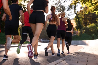 Group of people running outdoors on sunny day, back view