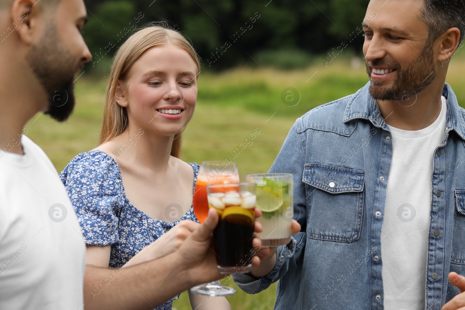 Photo of Happy friends clinking glasses with cocktails outdoors