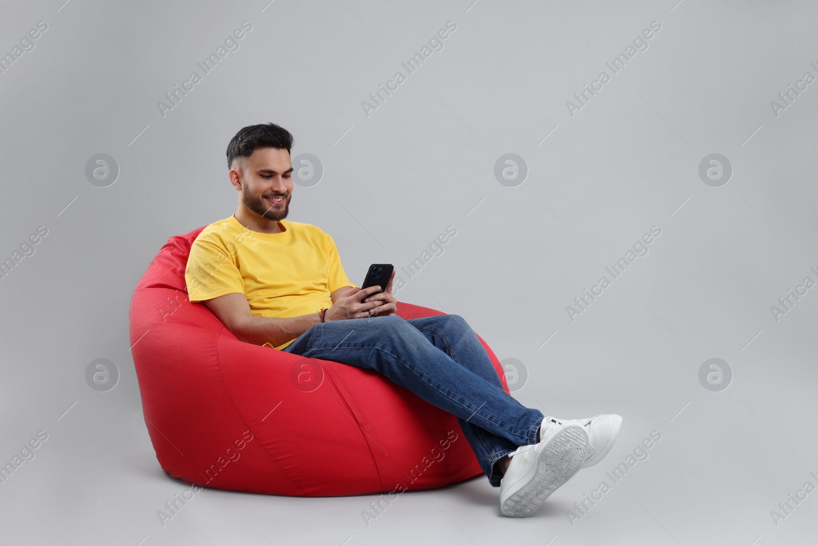 Photo of Happy young man using smartphone on bean bag chair against grey background, space for text