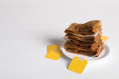 Photo of Saucer with used tea bags on white wooden table. Space for text