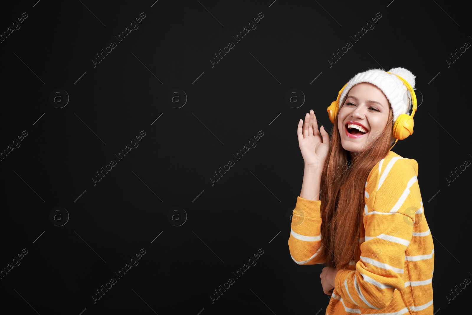 Photo of Young woman listening to music with headphones on black background, space for text