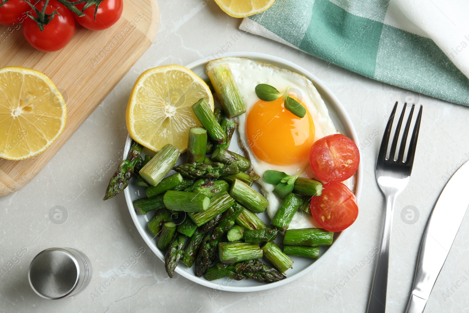 Photo of Oven baked asparagus served with fried egg on light grey marble table, flat lay