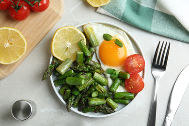 Photo of Oven baked asparagus served with fried egg on light grey marble table, flat lay