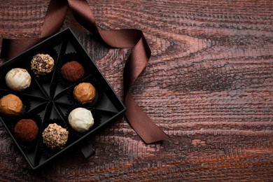 Photo of Box of tasty chocolate candies and ribbon on wooden table, flat lay. Space for text