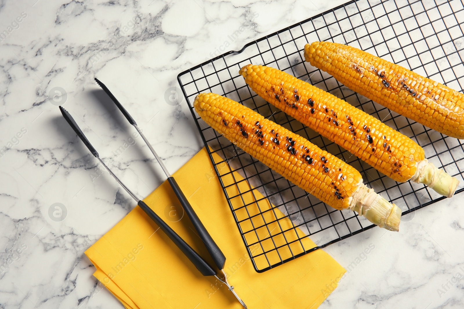 Photo of Cooling rack with grilled corn cobs on marble background, top view