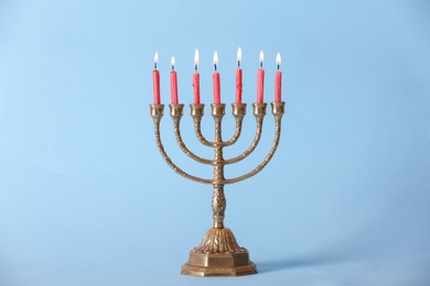 Golden menorah with burning candles on light blue background