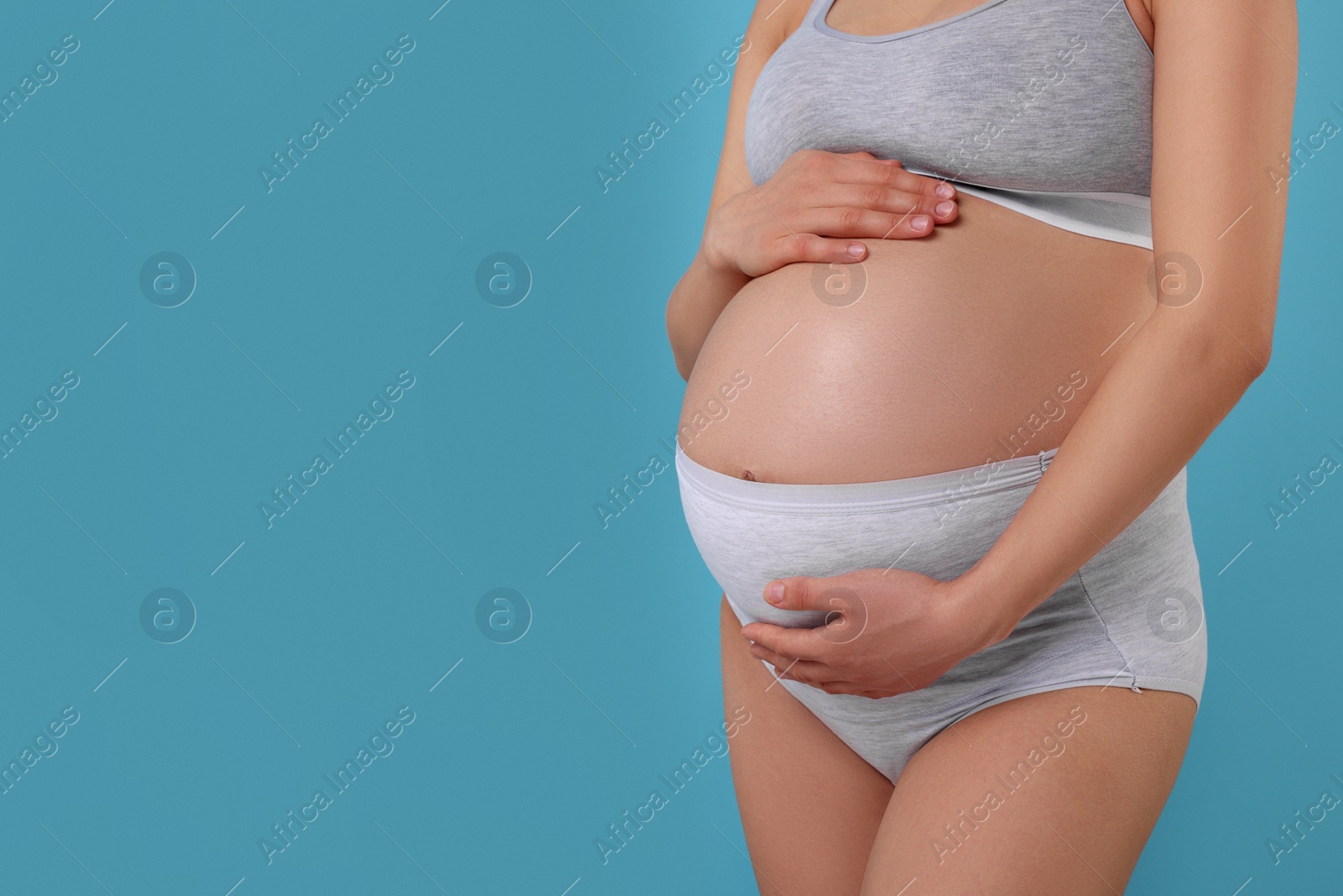 Photo of Pregnant woman in comfortable maternity underwear on light blue background, closeup. Space for text