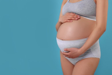 Pregnant woman in comfortable maternity underwear on light blue background, closeup. Space for text