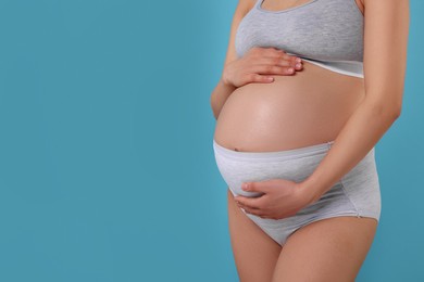 Photo of Pregnant woman in comfortable maternity underwear on light blue background, closeup. Space for text