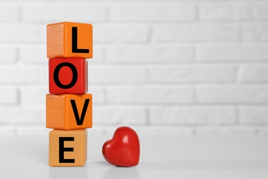Photo of Word Love made of wooden cubes with letters near red decorative heart on white table. Space for text