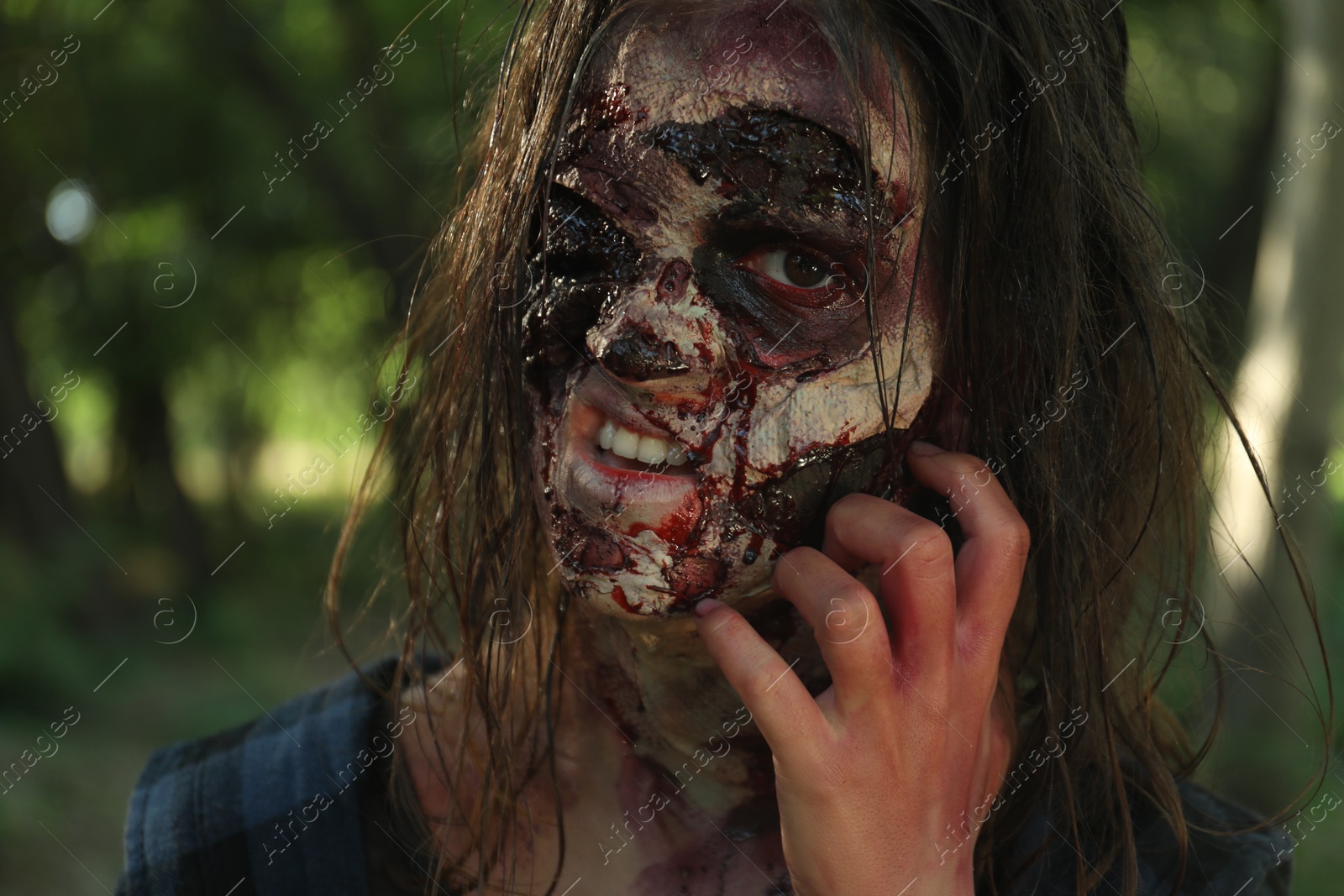 Photo of Scary zombie with bloody face outdoors, closeup. Halloween monster