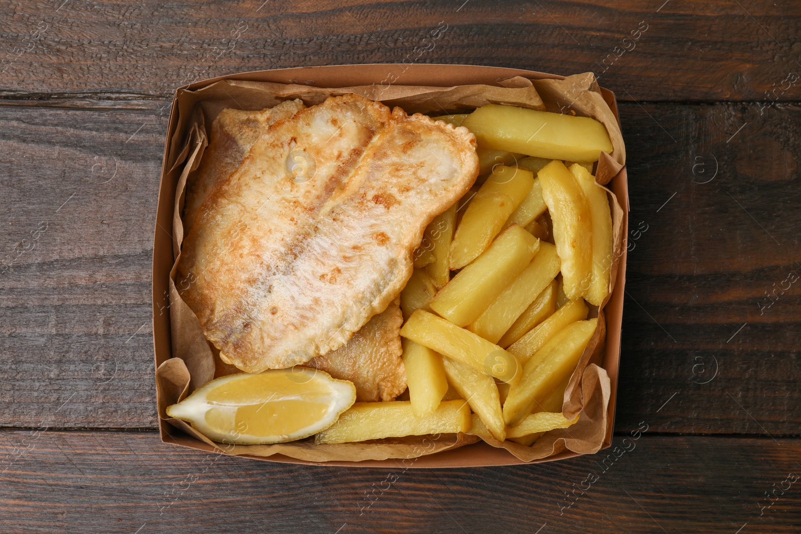 Photo of Delicious fish and chips in paper box on wooden table, top view
