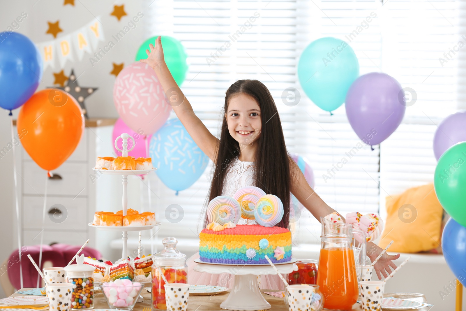 Photo of Happy girl at table with treats in room decorated for birthday party