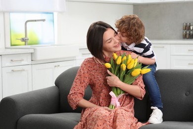 Photo of Little son congratulating his mom with Mother`s day at home, space for text. Woman holding bouquet of yellow tulips