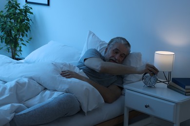 Photo of Sleepy senior man turning off alarm clock in bedroom