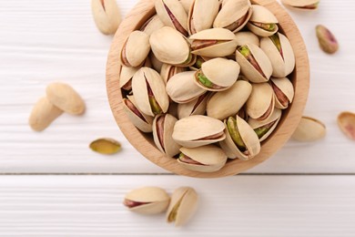 Tasty pistachios in bowl on white wooden table, top view