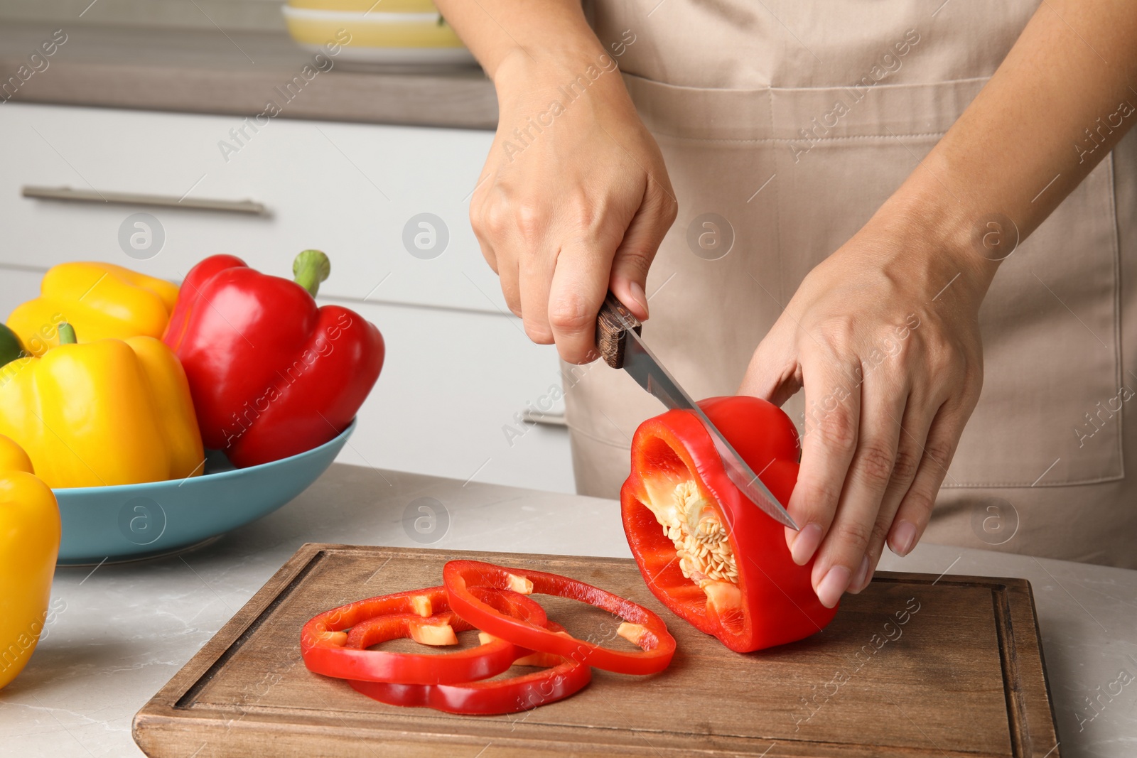 Photo of Woman cutting paprika pepper on wooden board at table, closeup