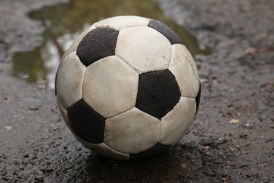 Photo of Dirty soccer ball near puddle on ground, closeup