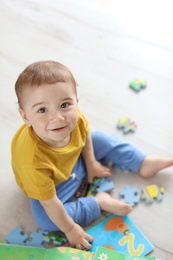 Adorable little boy playing with puzzle indoors