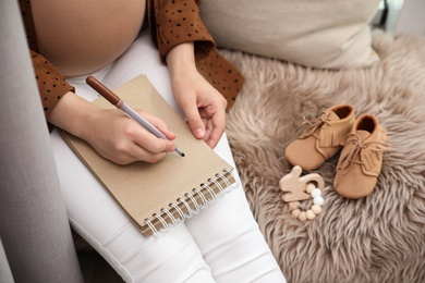 Photo of Pregnant woman writing baby names list at home, closeup