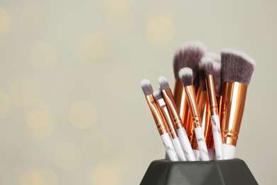 Photo of Set of makeup brushes in holder on light background. Space for text