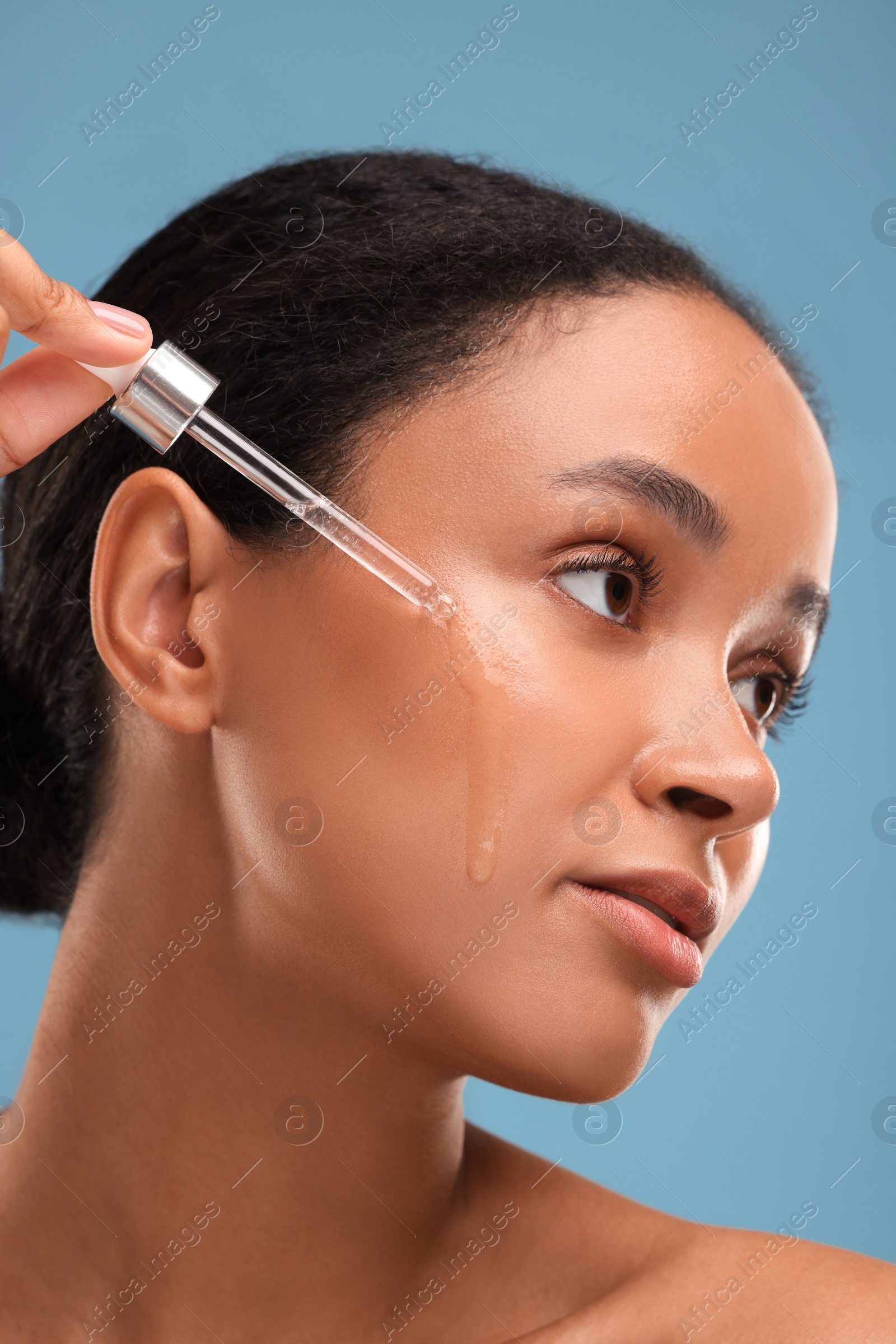 Photo of Beautiful woman applying serum onto her face on blue background