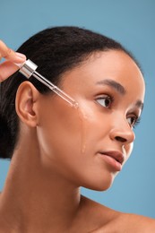 Beautiful woman applying serum onto her face on blue background