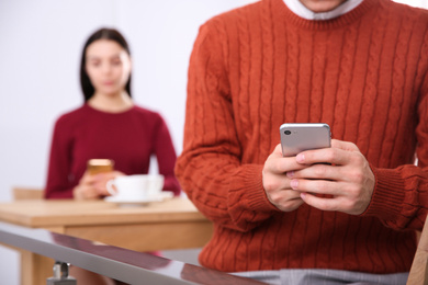 Photo of Man with smartphone ignoring his girlfriend in cafe, closeup. Relationship problems