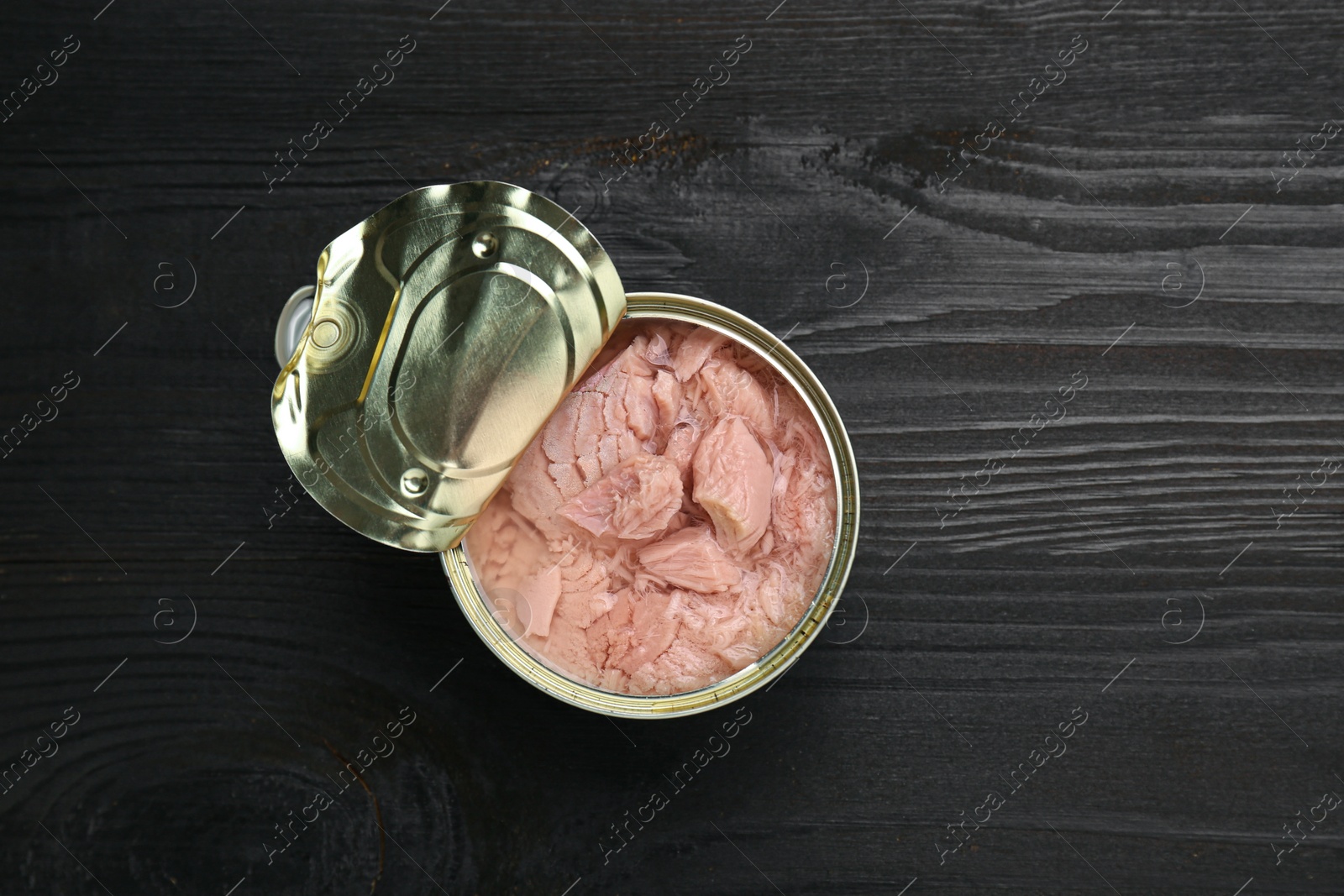 Photo of Tin can with canned tuna on black wooden table, top view. Space for text