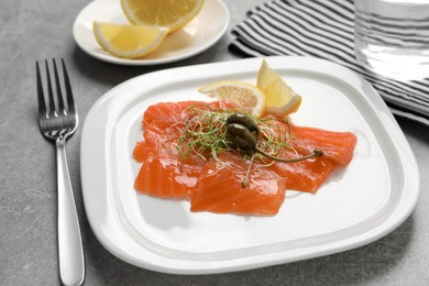 Salmon carpaccio with capers, microgreens and lemon served on grey table