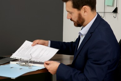 Businessman putting document into file folder at wooden table in office