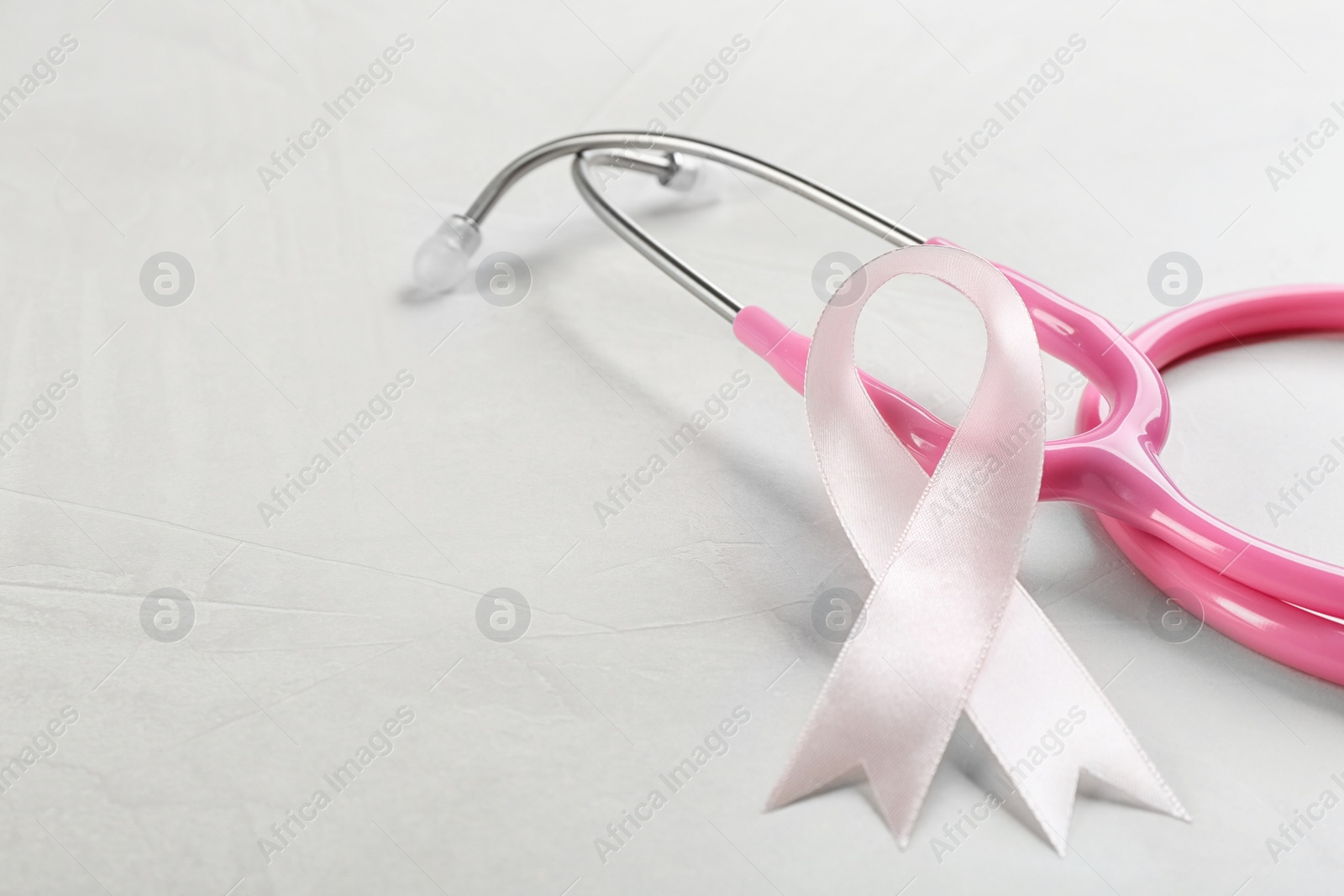 Photo of Pink ribbon and stethoscope on light grey stone background, closeup. Breast cancer concept