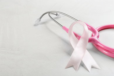 Pink ribbon and stethoscope on light grey stone background, closeup. Breast cancer concept