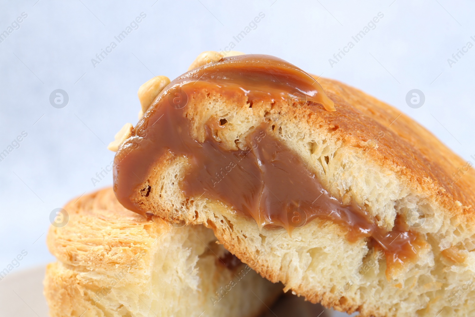 Photo of Supreme croissant with chocolate paste and nuts on light background, closeup. Tasty puff pastry