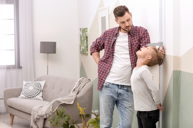 Photo of Young man measuring his son's height at home