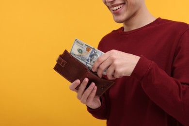 Happy man putting money into wallet on yellow background, closeup. Space for text