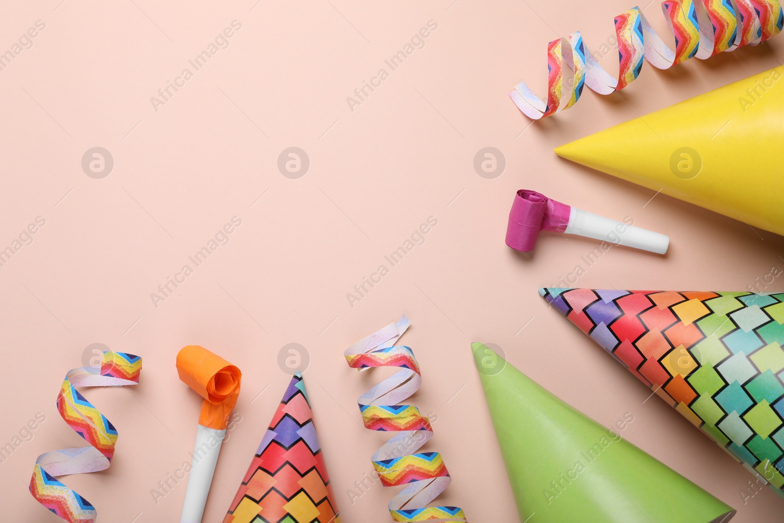 Photo of Flat lay composition with party hats and blowers on pale pink background, space for text. Birthday celebration