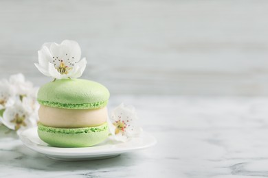 Photo of Green macaron and flowers on white marble table, space for text