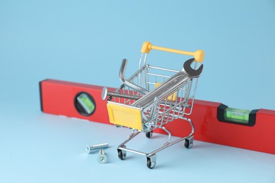 Photo of Shopping cart with different construction tools on light blue background