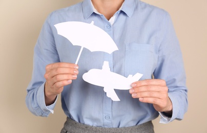 Photo of Insurance agent covering paper plane with umbrella cutout on color background, closeup. Travel safety concept