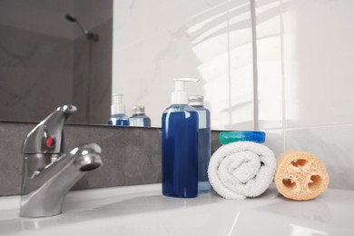 Photo of Loofah sponge, rolled towel and cosmetic products on sink in bathroom