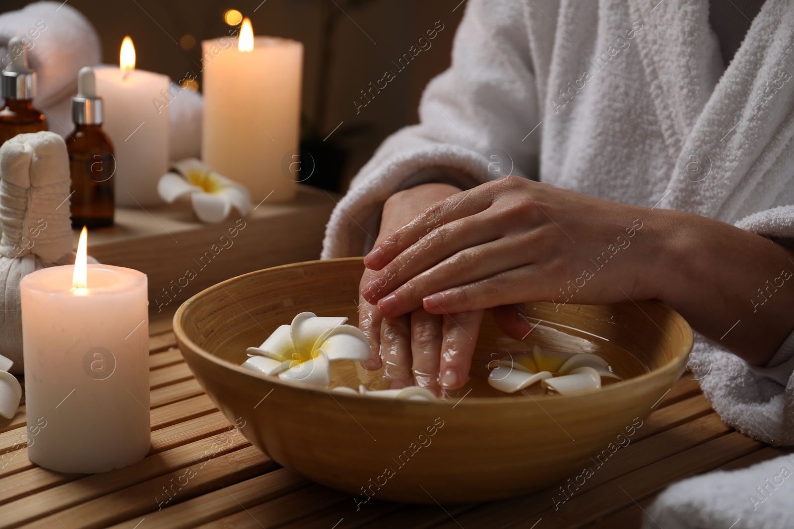 Photo of Woman soaking her hands in bowl of water and flowers at wooden table, closeup. Spa treatment