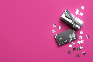 Photo of Gift card, present and confetti on pink background, flat lay. Space for text