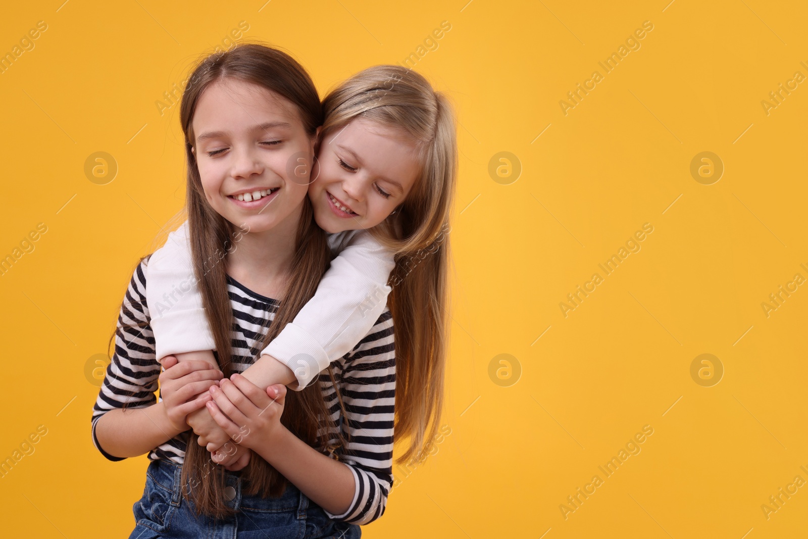 Photo of Portrait of cute little sisters on orange background, space for text