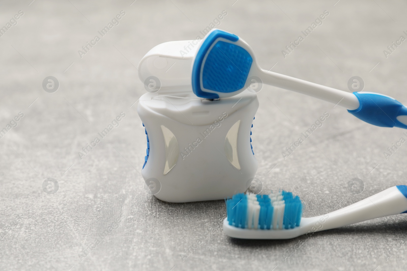 Photo of Blue tongue cleaner, toothbrush and dental floss on grey table, closeup