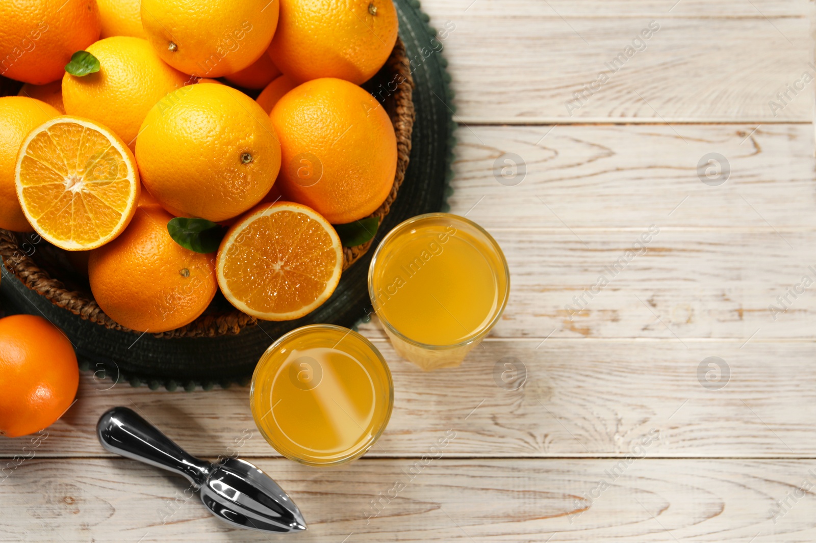 Photo of Many ripe juicy oranges, squeezer and fresh juice on white wooden table, flat lay. Space for text