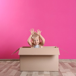 Cute little girl playing with cardboard box near color wall